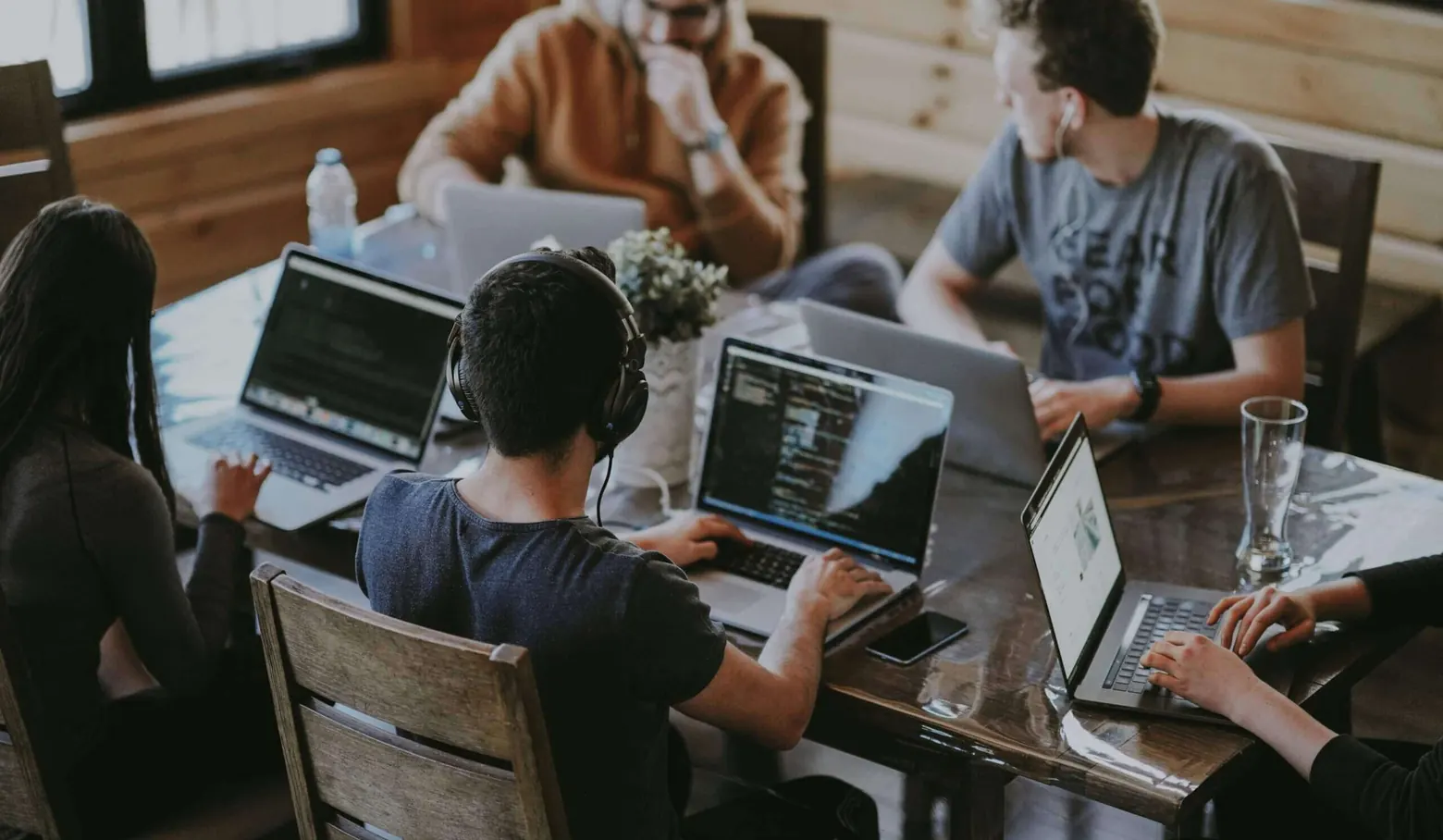 Mehrere Personen arbeiten gemeinsam an Laptops an einem Holztisch