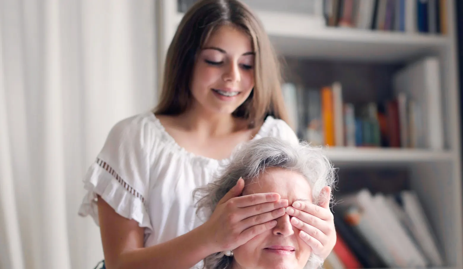 Junge Frau hält einer älteren Frau von hinten die Augen zu