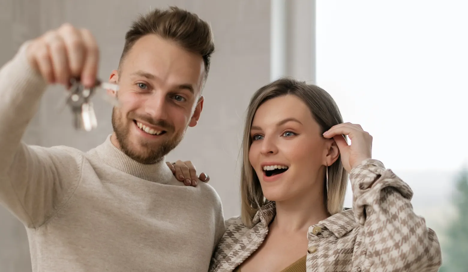 Junges Paar hält lachend einen Wohnungsschlüssel hoch