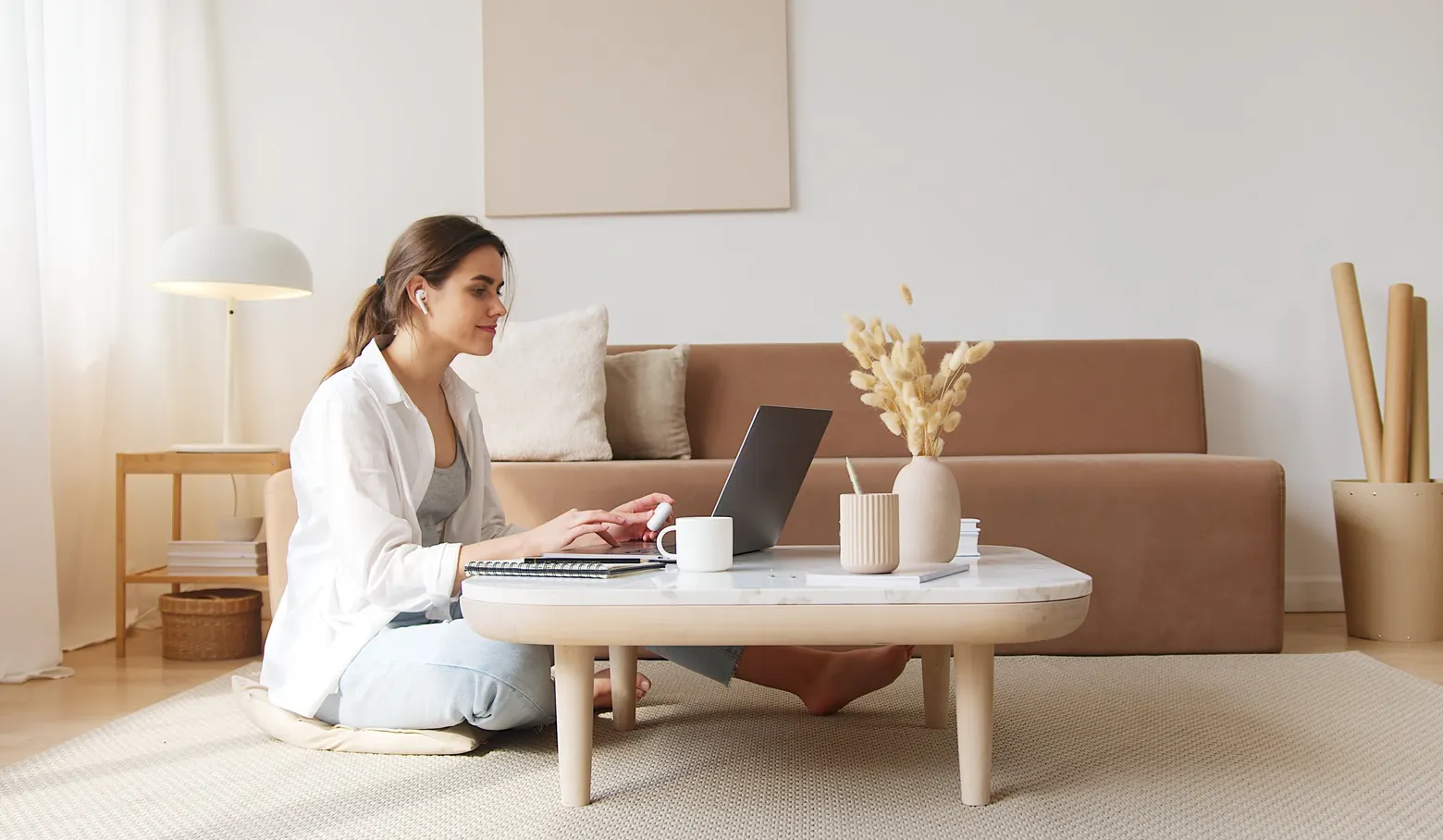 Frau arbeitet im Wohnzimmer am Laptop auf einem niedrigen Couchtisch