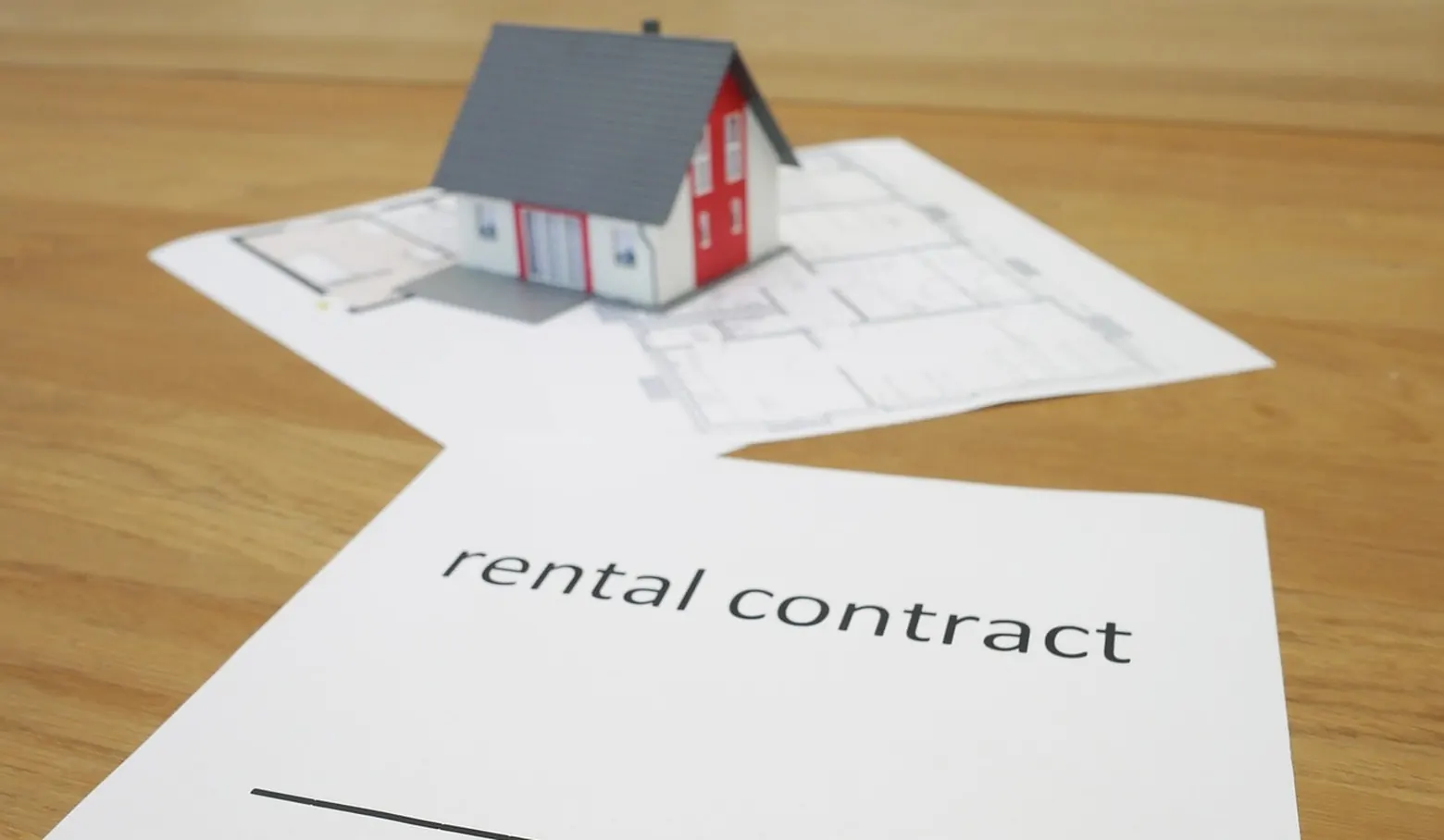Hausmodell auf einem Grundriss, davor ein Blatt mit der Aufschrift „rental contract“